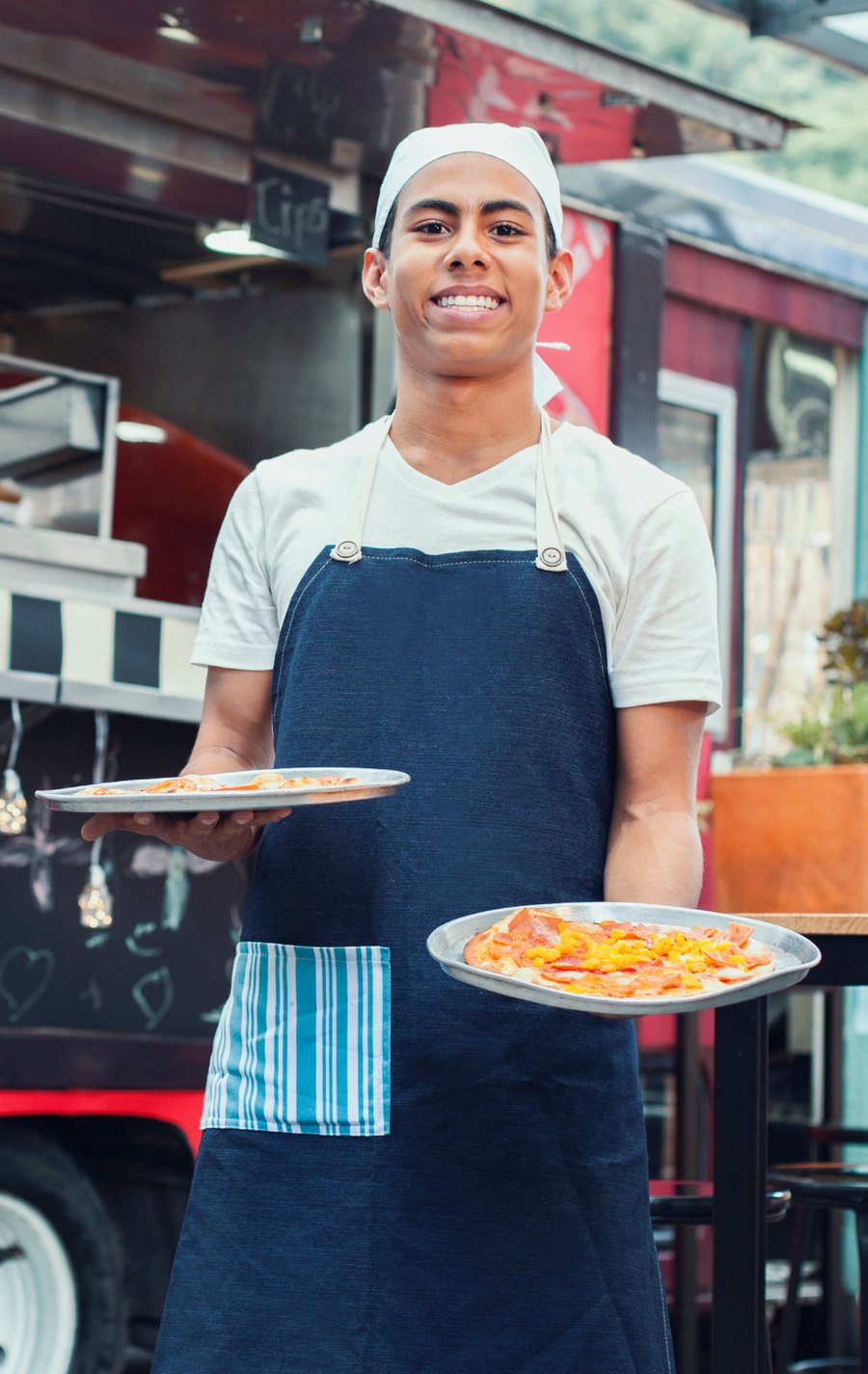 Joven emprendedor con delantal sirviendo dos platos frente a su food truck